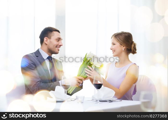 restaurant, couple and holiday concept - smiling man giving girlfriend or wife bouquet of flowers at restaurant