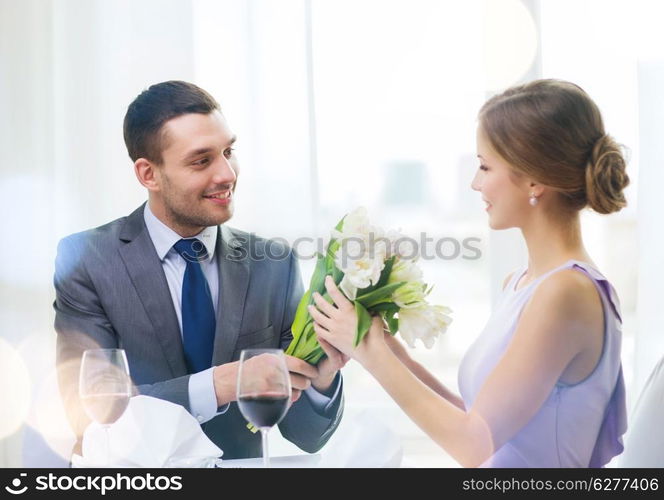 restaurant, couple and holiday concept - smiling man giving girlfriend or wife bouquet of flowers at restaurant