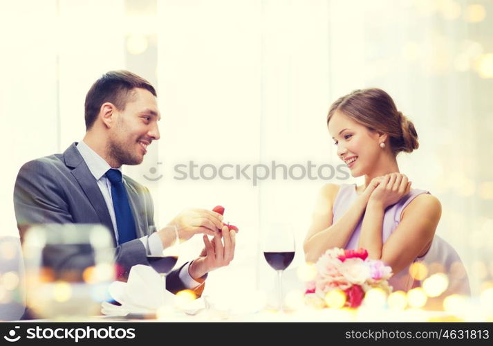 restaurant, couple and holiday concept - smiling man proposing to his girlfriend at restaurant