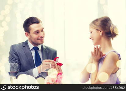 restaurant, couple and holiday concept - smiling man proposing to his girlfriend at restaurant