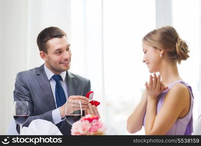 restaurant, couple and holiday concept - smiling man proposing to his girlfriend at restaurant