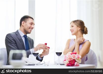 restaurant, couple and holiday concept - smiling man proposing to his girlfriend at restaurant