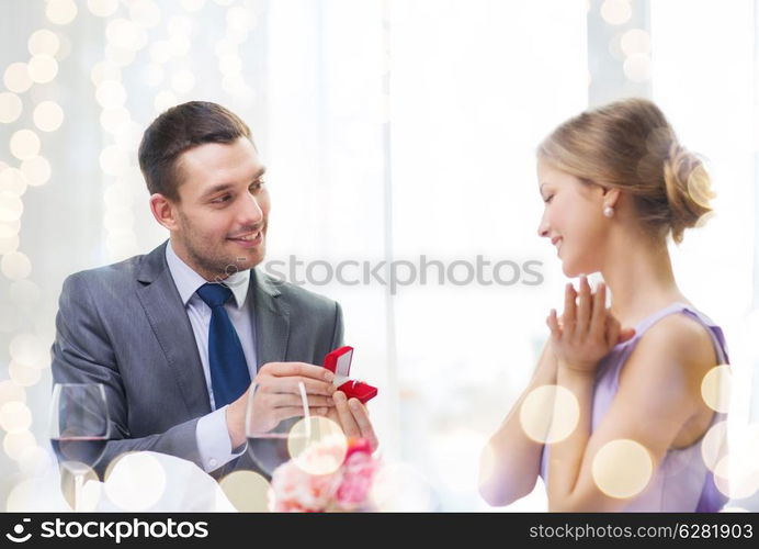 restaurant, couple and holiday concept - smiling man proposing to his girlfriend at restaurant