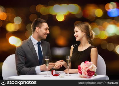 restaurant, couple and holiday concept - smiling man putting on finger engagement ring at restaurant