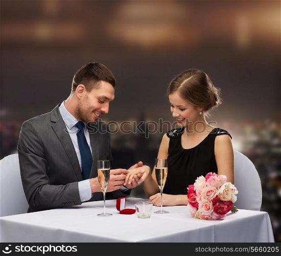 restaurant, couple and holiday concept - smiling man putting on finger engagement ring at restaurant
