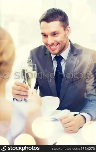 restaurant, couple and holiday concept - smiling man with glass of champagne looking at wife or girlfriend at restaurant