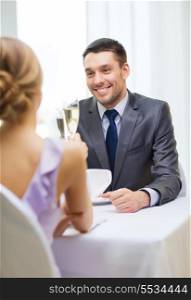 restaurant, couple and holiday concept - smiling man with glass of champagne looking at wife or girlfriend at restaurant