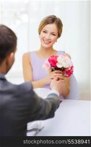 restaurant, couple and holiday concept - smiling woman recieving bouquet of flowers from husband or boyfriend at restaurant