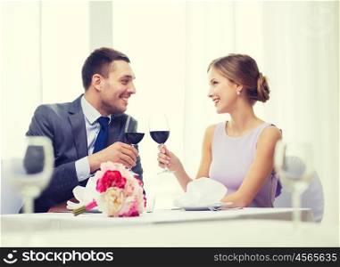 restaurant, couple and holiday concept - smiling young couple with glasses of red wine looking at each other at restaurant