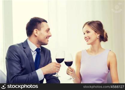 restaurant, couple and holiday concept - smiling young couple with glasses of red wine looking at each other at restaurant