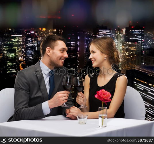 restaurant, couple and holiday concept - smiling young couple with glasses of red wine looking at each other at restaurant