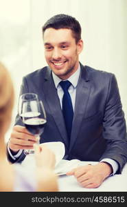 restaurant, couple and holiday concept - smiling young man with glass of red wine looking at girlfriend or wife at restaurant