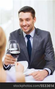 restaurant, couple and holiday concept - smiling young man with glass of red wine looking at girlfriend or wife at restaurant