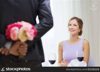restaurant, couple and holiday concept - smiling young woman looking at man with flower bouquet behind the back