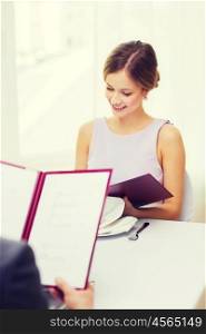 restaurant, couple and holiday concept - smiling young woman looking at menu at restaurant