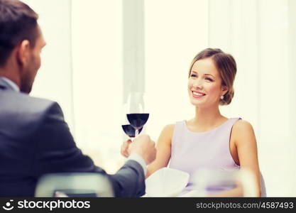 restaurant, couple and holiday concept - smiling young woman with glass of red wine looking at boyfriend or husband at restaurant