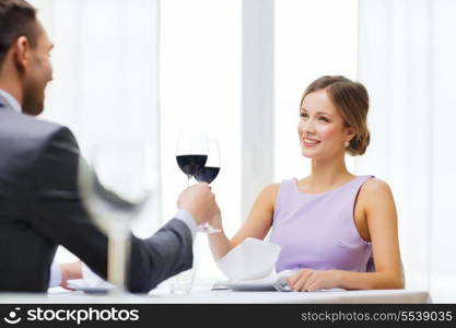 restaurant, couple and holiday concept - smiling young woman with glass of red wine looking at boyfriend or husband at restaurant