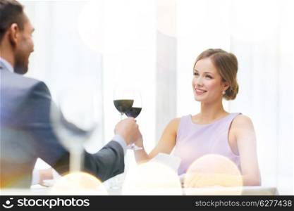 restaurant, couple and holiday concept - smiling young woman with glass of red wine looking at boyfriend or husband at restaurant