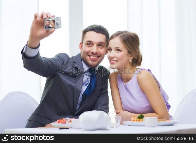 restaurant, couple, technology and holiday concept - smiling couple taking self portrait picture with digital camera at resaturant