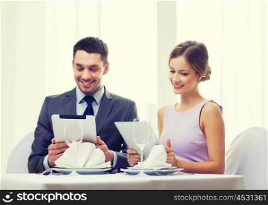 restaurant, couple, technology and holiday concept - smiling couple with menus on tablet pc computers at restaurant