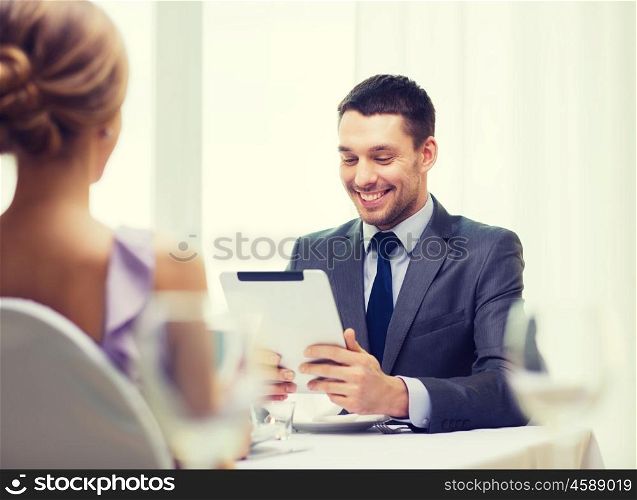 restaurant, couple, technology and holiday concept - smiling man looking at menu on tablet pc computer at restaurant
