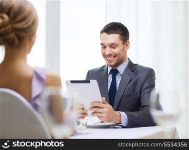 restaurant, couple, technology and holiday concept - smiling man looking at menu on tablet pc computer at restaurant