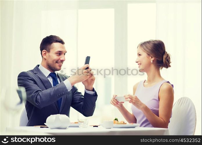 restaurant, couple, technology and holiday concept - smiling man taking picture of wife or girlfriend while picturing sushi with smartphone