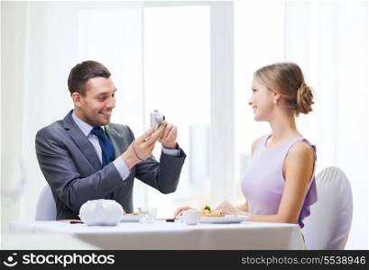 restaurant, couple, technology and holiday concept - smiling man taking picture of wife or girlfriend with digital camera at restaurant