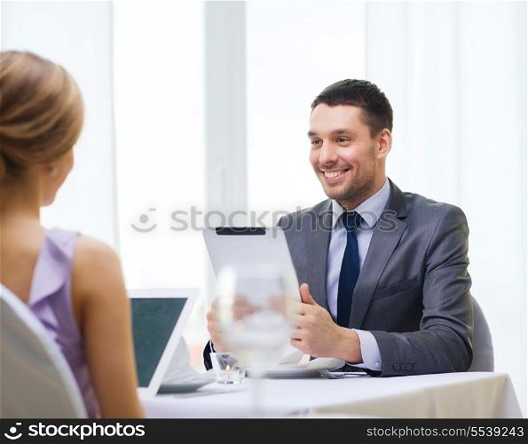 restaurant, couple, technology and holiday concept - smiling man with tablet pc computer looking at wife or girlfriend at reastaurant