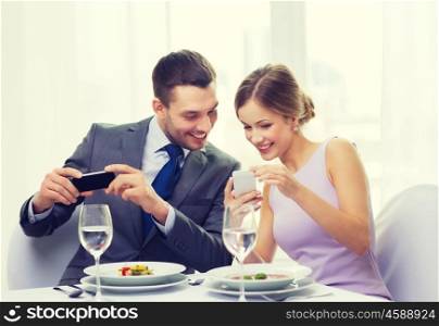 restaurant, couple, technology and holiday concept - smiling woman showing picture to husband or boyfriend on smartphone at restaurant
