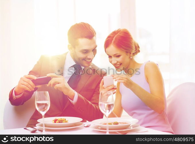 restaurant, couple, technology and holiday concept - smiling woman showing picture to husband or boyfriend on smartphone at restaurant