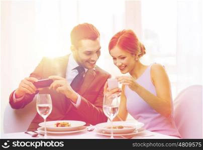 restaurant, couple, technology and holiday concept - smiling woman showing picture to husband or boyfriend on smartphone at restaurant