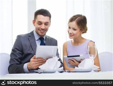 restaurant, couple, technology and holiday concept - smiling young woman looking into boyfriends or husbands menu on tablet pc computer