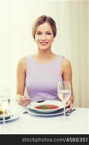 restaurant, people and holiday concept - smiling young woman eating appetizer at restaurant