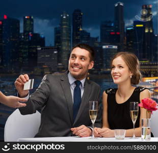 restaurant, people and holidays concept - smiling couple paying for dinner with credit card at restaurant over night city background