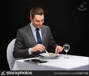 restaurant, people, technology and holiday concept - smiling man with tablet pc eating main course at restaurant