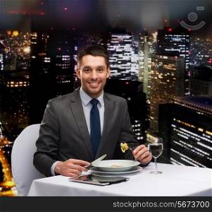 restaurant, people, technology and holiday concept - smiling man with tablet pc eating main course at restaurant