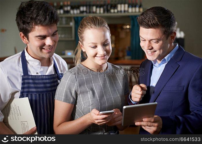 Restaurant Team Discussing Menu Looking At Digital Tablet
