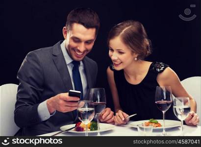 restaurant, technology, couple and holiday concept - smiling couple taking picture of main course with smartphone camera at restaurant