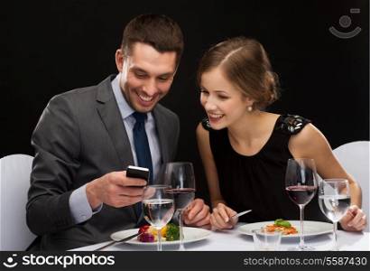 restaurant, technology, couple and holiday concept - smiling couple taking picture of main course with smartphone camera at restaurant