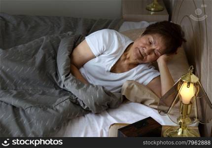 Restless senior woman staring at bed stand during night time. Insomnia concept.