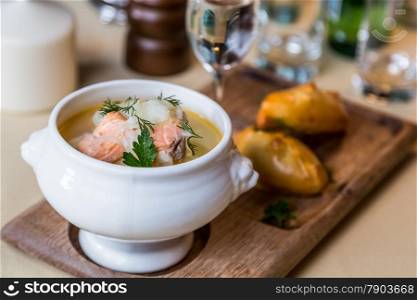 Restourant serving dish - salmon soup on wooden board with pie, drink on table