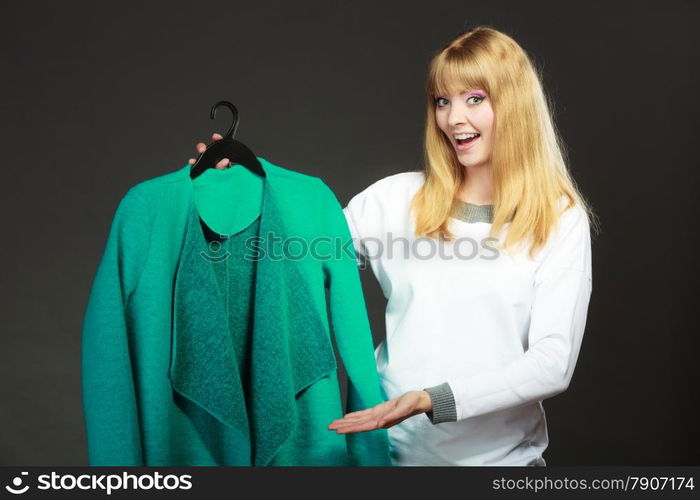 Retail and sale. Blonde girl fashionable woman buying clothes. Client customer holding hanger with green coat dark background