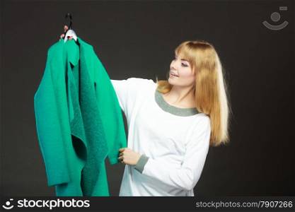 Retail and sale. Blonde girl fashionable woman buying clothes. Client customer holding hanger with green coat dark background