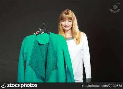 Retail and sale. Blonde girl fashionable woman buying clothes. Client customer holding hanger with green coat dark background