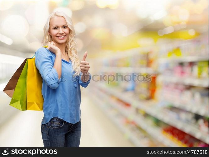 retail, people, gesture and sale concept - smiling woman with many shopping bags showing thumbs up over supermarket background