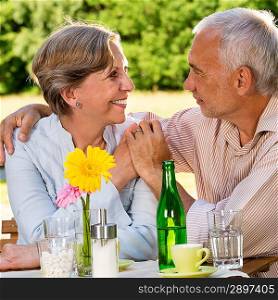 Retired couple sitting at table holding hands outdoors