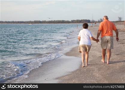 Retired couple walking hand in hand on the beach. Rear view.
