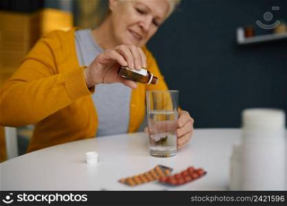 Retired elderly woman dripping medical sedative drops in glass with water. Healthcare and treatment. Retired elderly woman dripping medical sedative drops