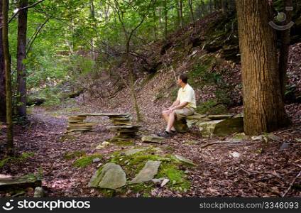 Retired hiker rests on stone benches in a clearing in a forest on a hike
